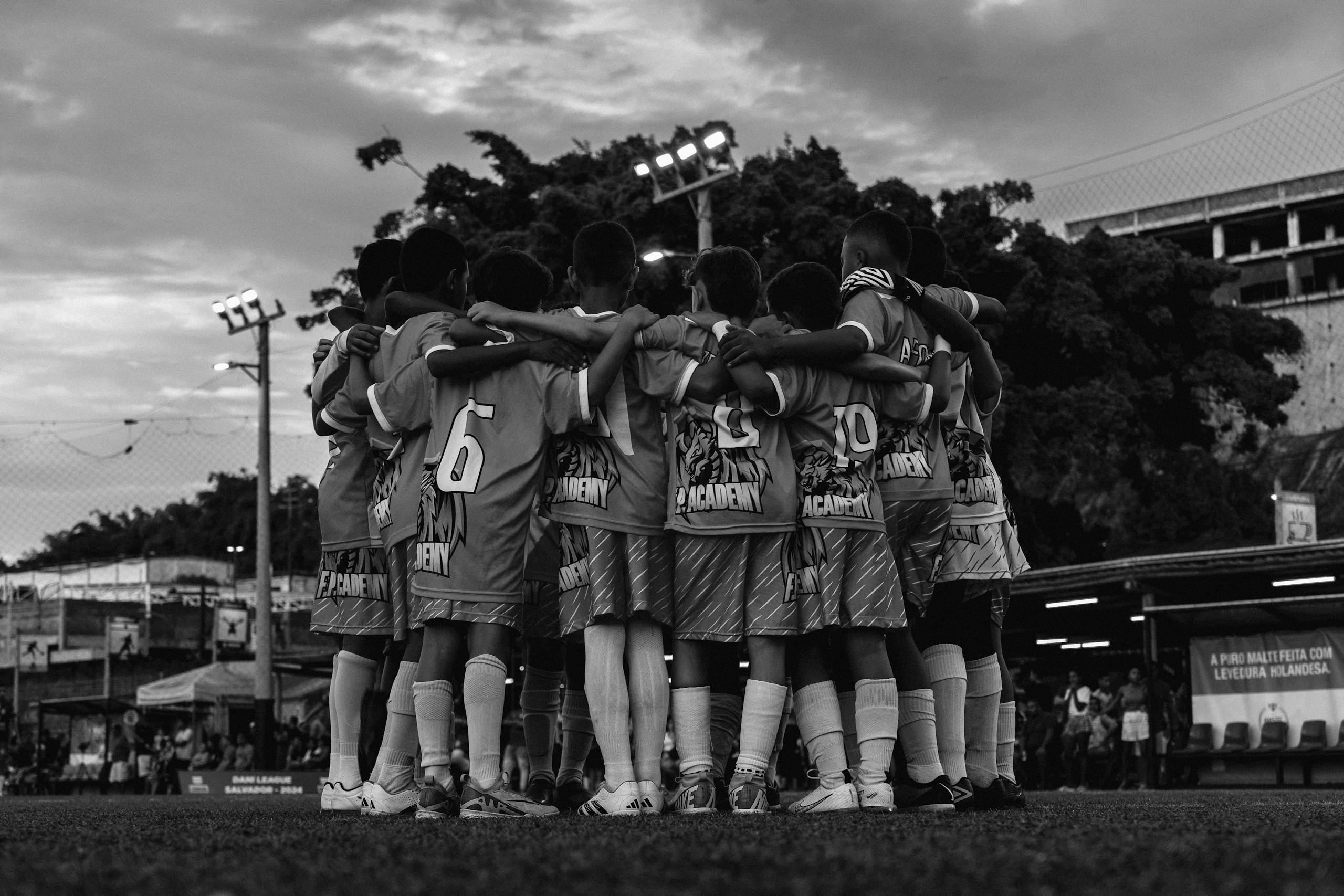 A black and white photo of a youth soccer team huddling on the field during dusk.