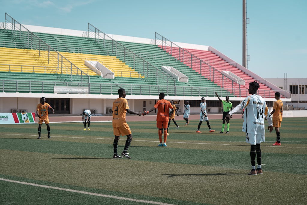 Energetic football match with players in orange and white, vibrant stadium backdrop.