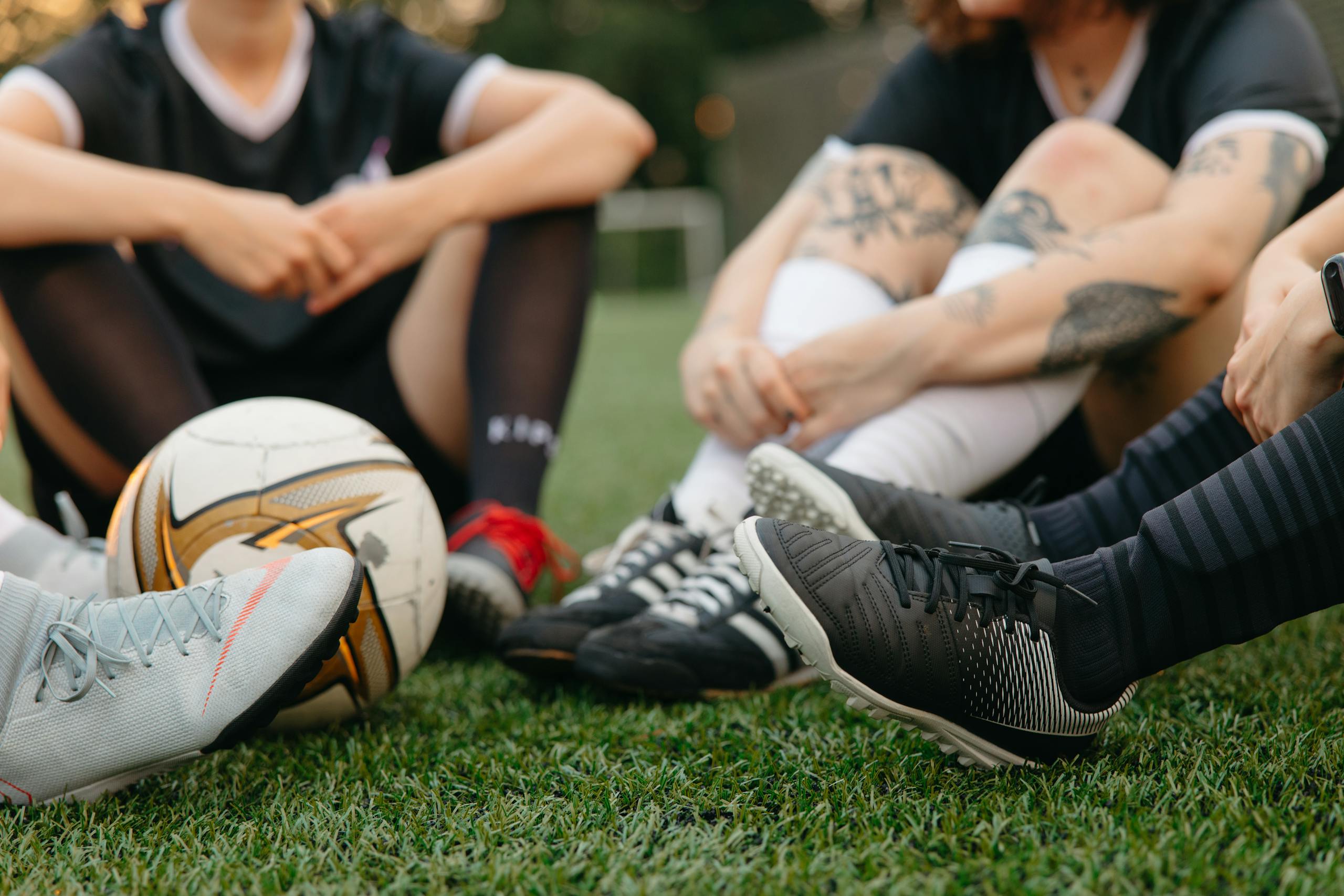 Soccer players sit together with a football on a lush green pitch, showing camaraderie.